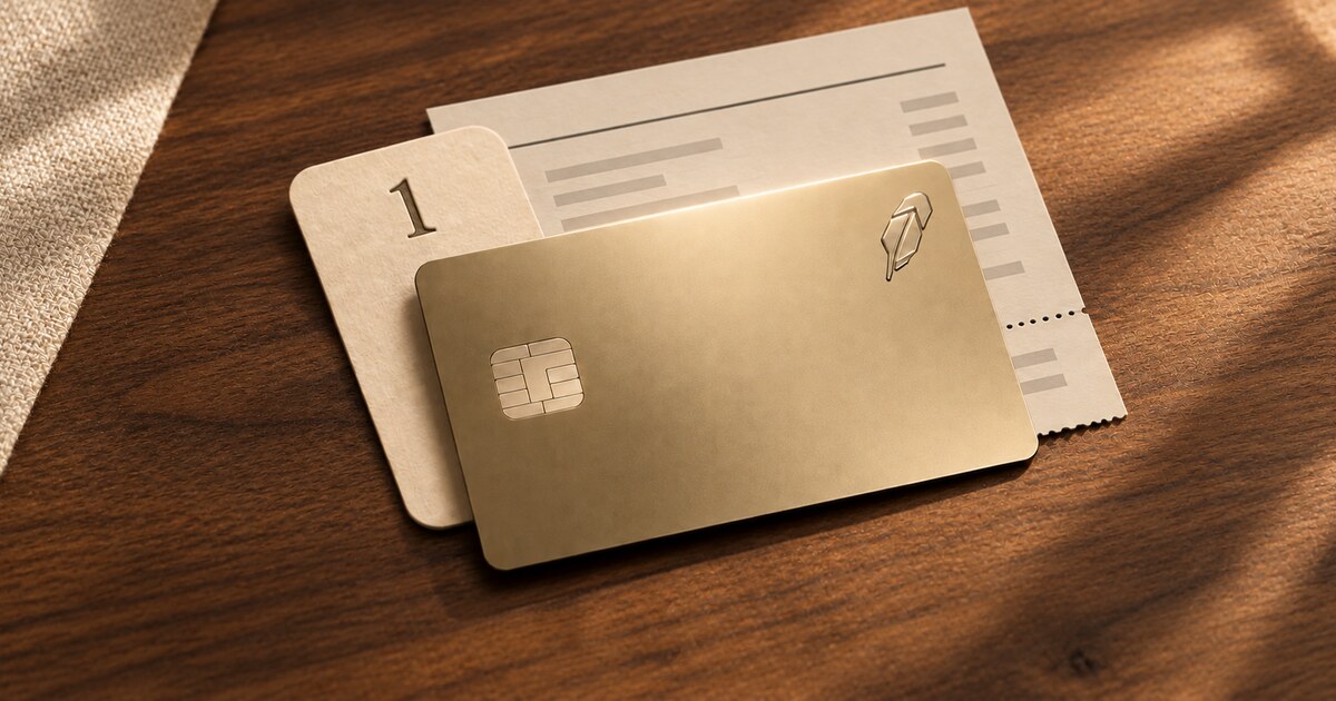 A bright gold Robinhood credit card over a cream bill and calendar tab marked 1 on a warm wooden desk.